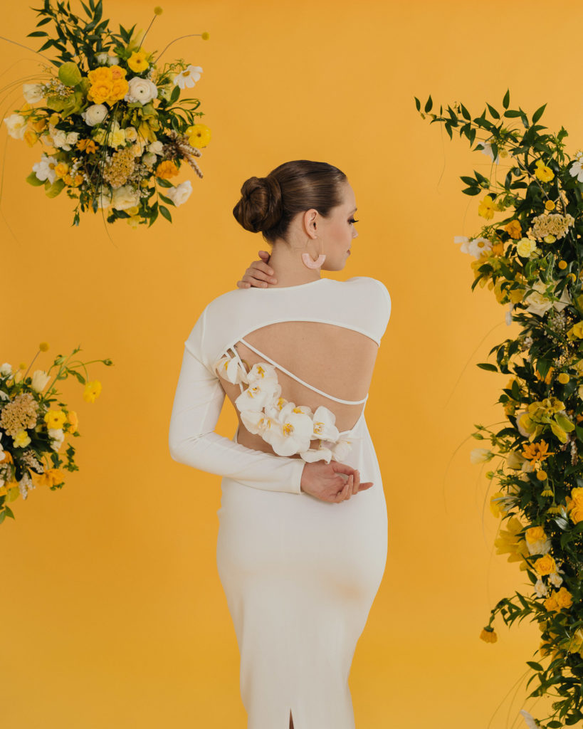 sleek-wedding-gown-with-floral-open-back-updo-in-studio-yellow-backdrop