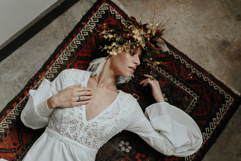bohomenian-bride-laying-on-persian-rug-wearing-yellow-red-flower-crown-long-sleeve-wedding-dress