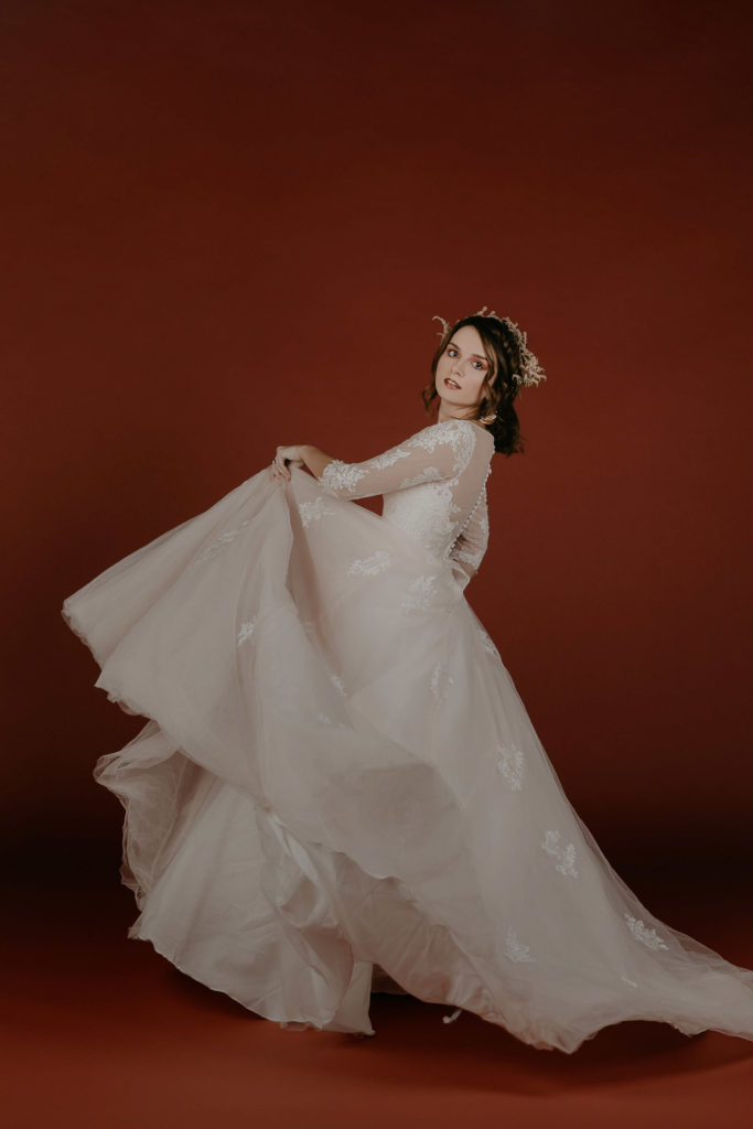 bride-spinning-large-ballroom-wedding-dress-wearing-white-flower-crown-on-red-backdrop