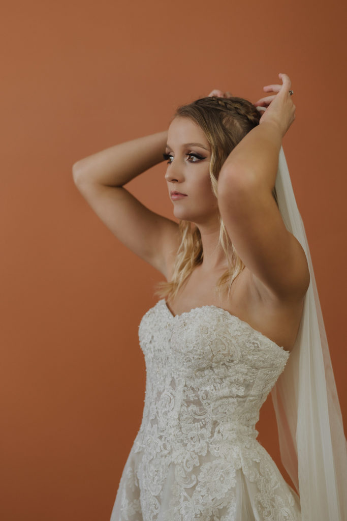 bride-wearing-strapless-wedding-dress-with-cathedral-veil-against-terracotta-background