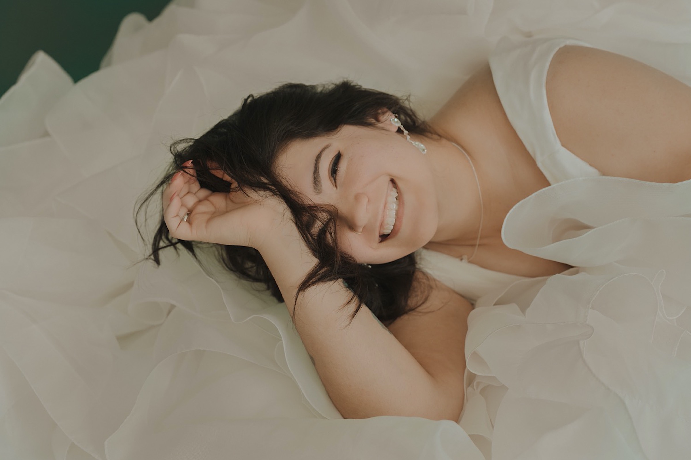 bride-laying-in-layered-wedding-dress-with-arms-over-head-smiling-head-to-side